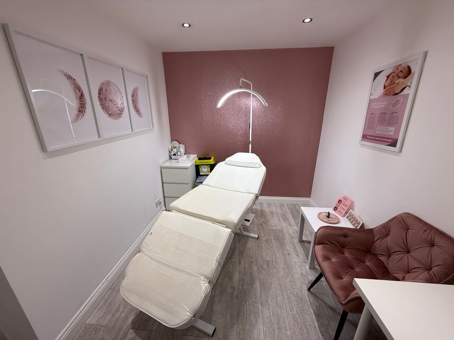 Danielle's treatment room: a white couch under an arched lamp, framed pink prints and a velvet chair, in front of a rose glitter wall